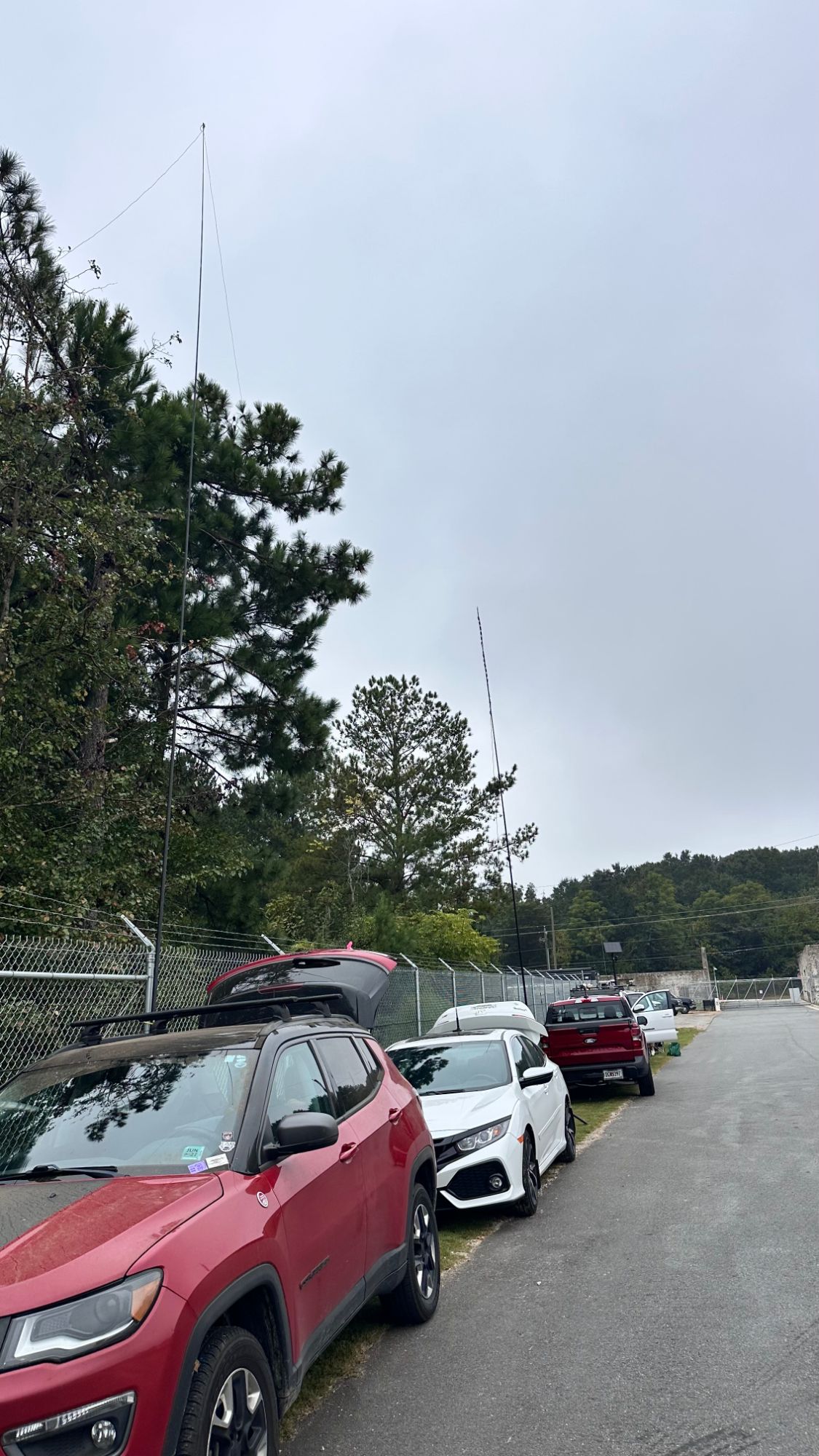 Two tall HF antennas raised above parked vehicles against an overcast sky