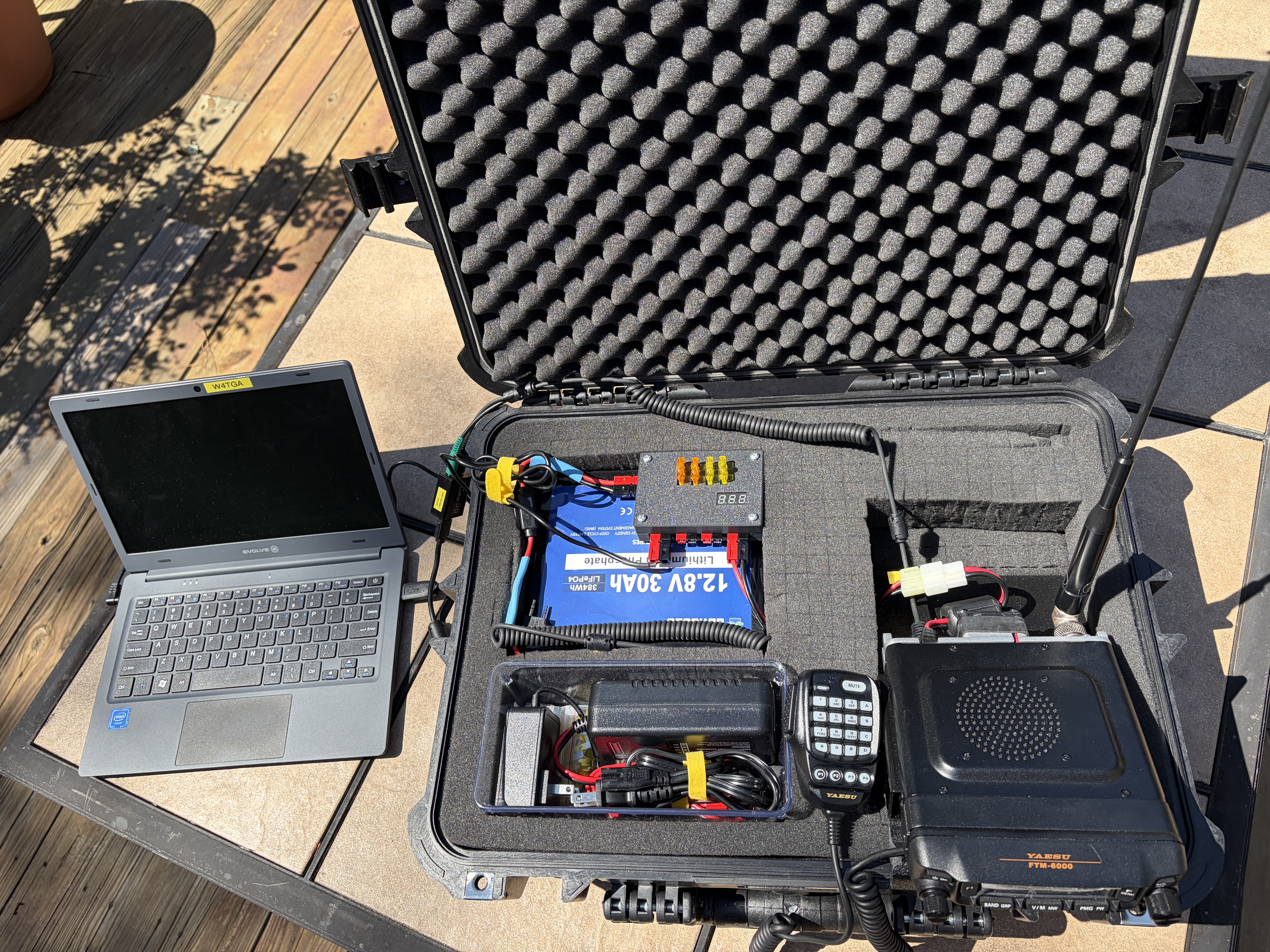 W4TGA's go-kit deployed — laptop set up next to the open case, Yaesu FTM-6000 mobile radio and battery visible inside, antenna ready to attach.